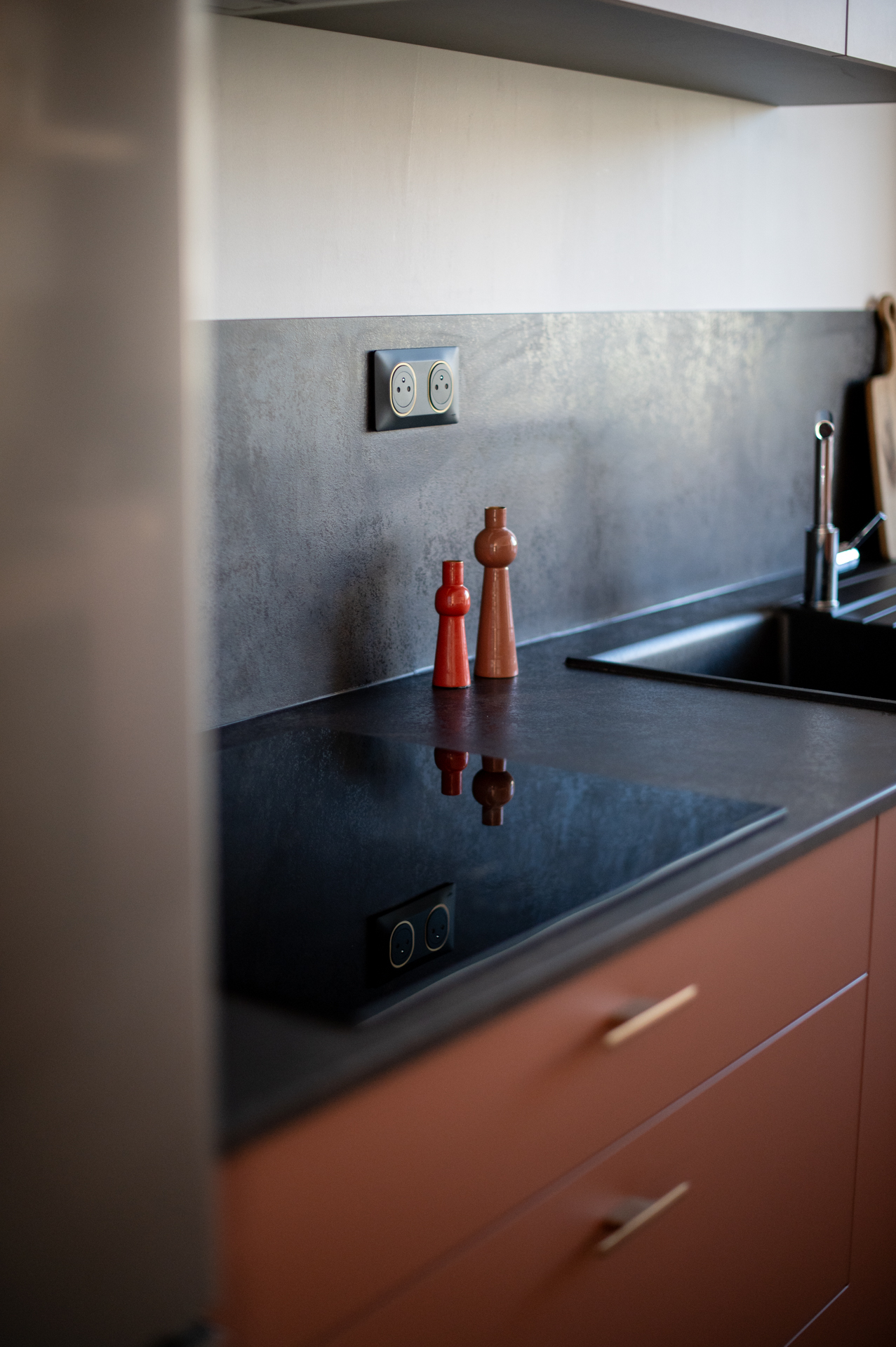 Gros plan sur un plan de travail noir avec plaque de cuisson intégrée et robinet, dans une cuisine terracotta réalisée par L'Atelier d'Agencement.