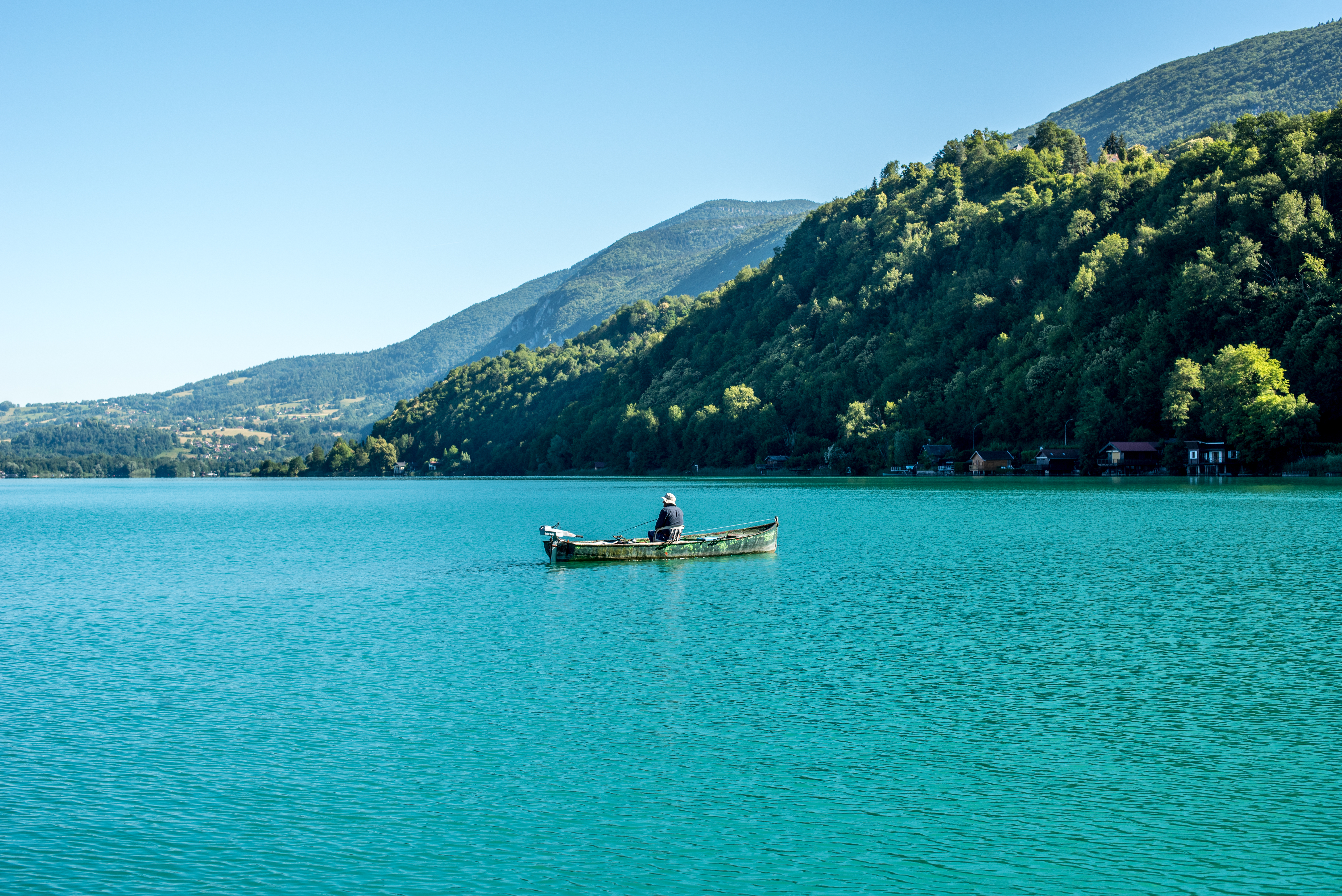 Une barque de pêcheur sur les eaux turquoise du lac d'Aiguebelette, entourée de collines boisées, en Savoie.