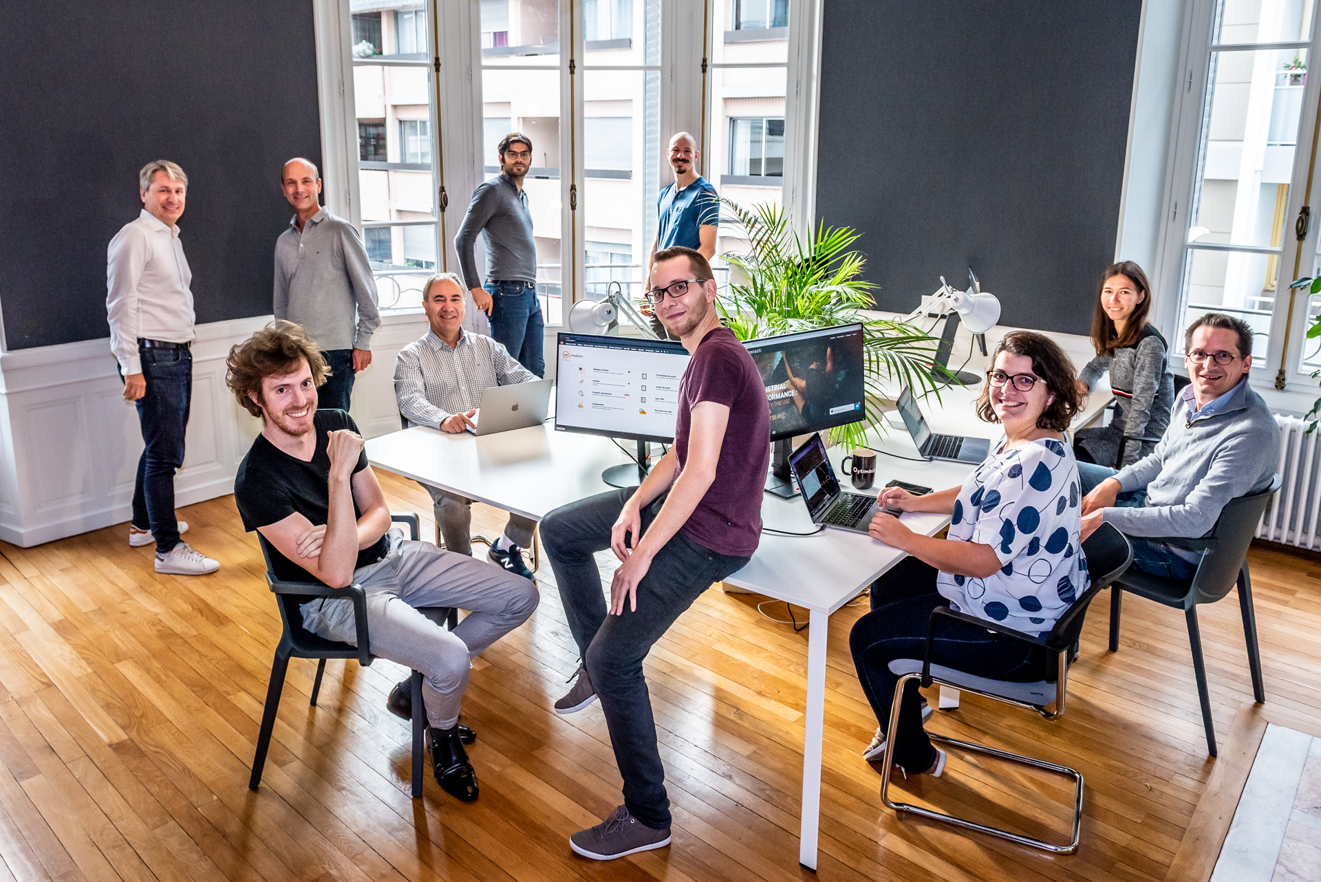 Photo d'équipe d'une entreprise dans son open space lumineux, plusieurs collaborateurs autour de leurs postes de travail, réalisée par Pict'Your Company