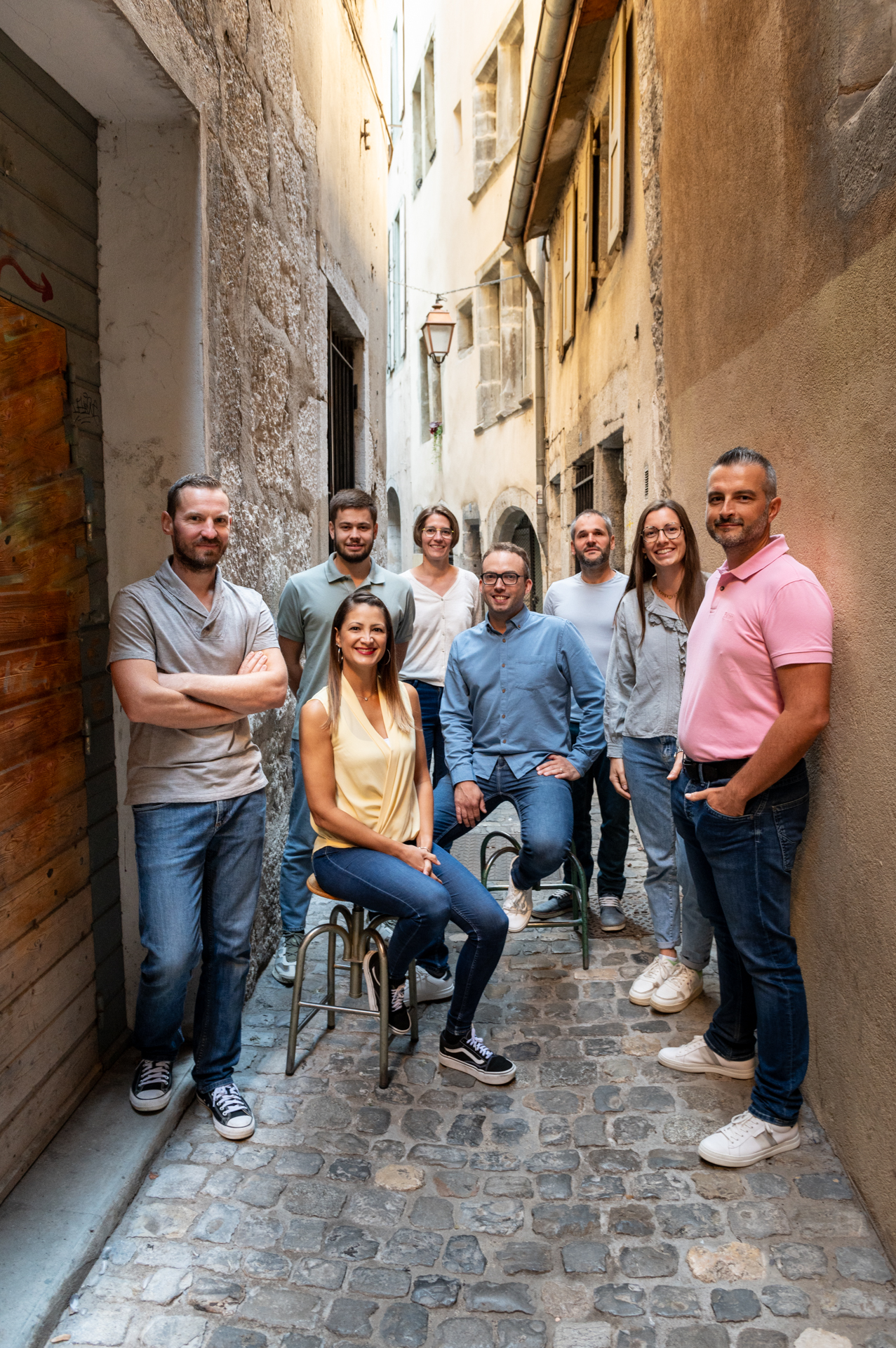 Photo de groupe de l'équipe d'Eureka Géomètres Experts, huit personnes debout et assises dans une ruelle pavée de la vieille ville de Chambéry, entre des façades en pierre.