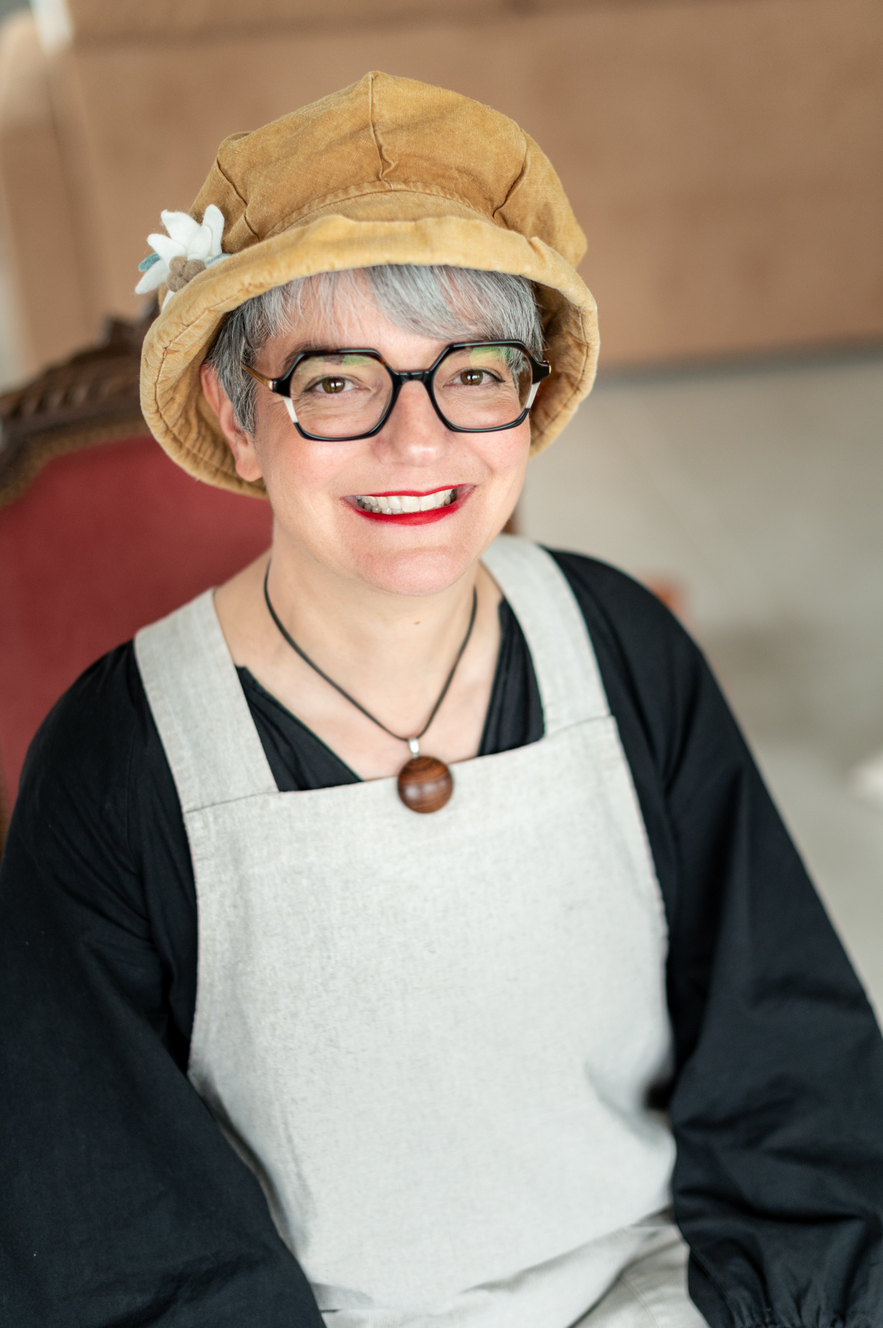 Portrait souriant d'Andréane, conteuse, coiffée d'un chapeau et vêtue de son costume de scène, dans un décor chaleureux.