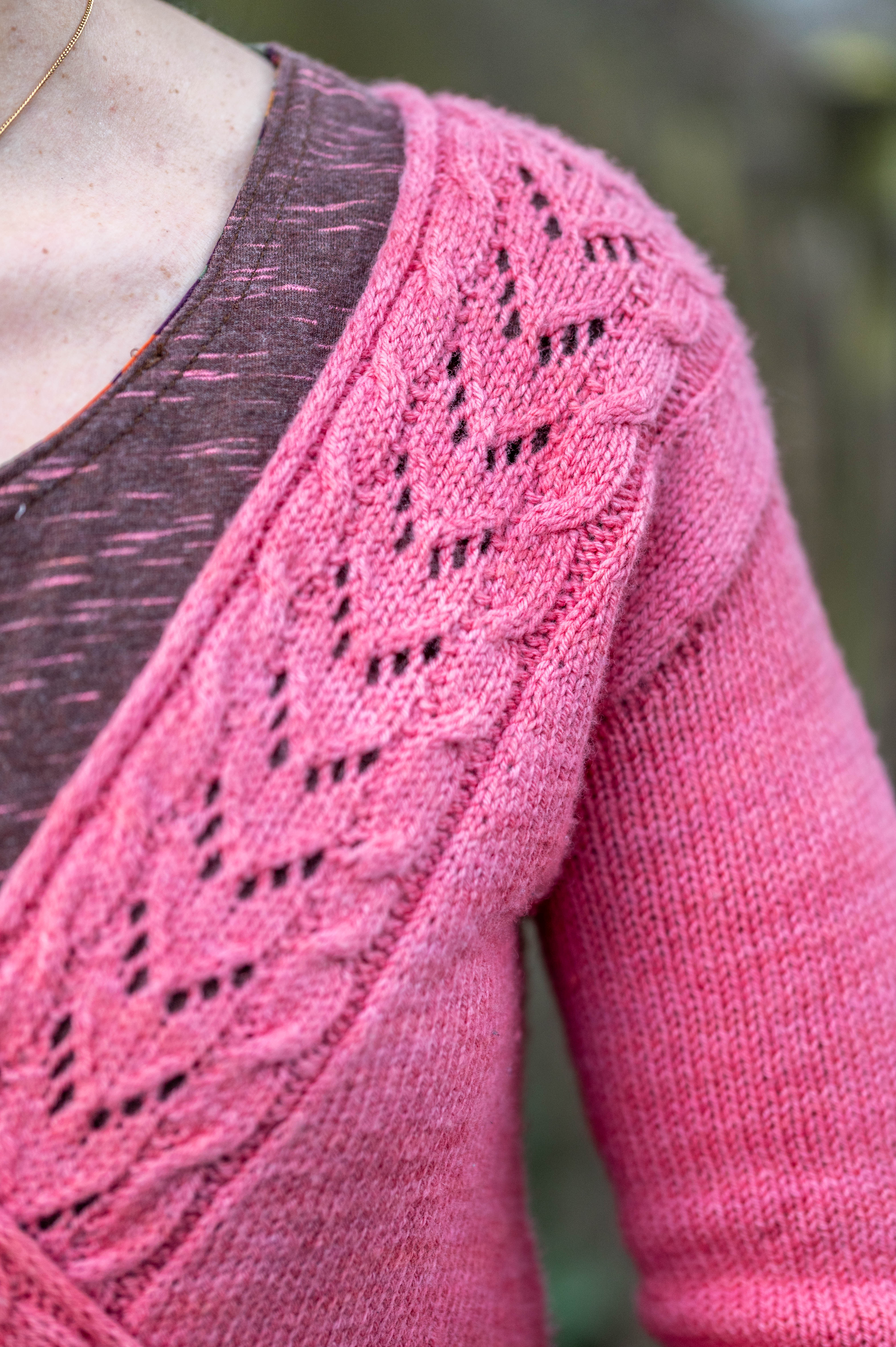 Gros plan sur un gilet croisé en tricot rose framboise avec des motifs ajourés en forme de feuilles, création de la marque Mlle Pétronille.